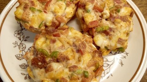 Auf einem Teller liegen drei goldbraune Pizzabrötchen, die mit Käse und Schinken belegt sind, auf einem Holztisch.
