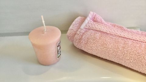 Eine rosa Duftkerze steht auf einem Waschbecken neben einem gefalteten, rosa Handtuch und schafft eine entspannende Atmosphäre.