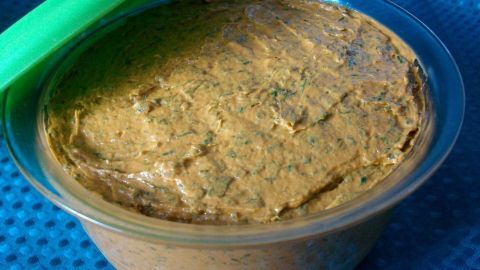 Eine cremige Tomatenbutter steht in einem durchsichtigen Behälter auf einem blauen Untergrund und wartet auf Verwendung.