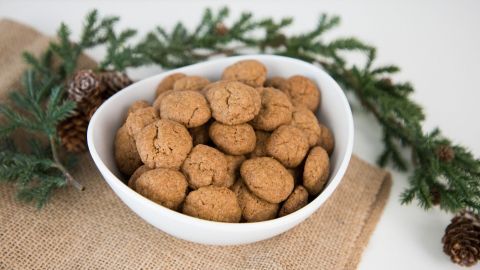Runde, goldbraune Pfeffernüsse liegen in einer weißen Schüssel, umgeben von weihnachtlichem Tannengrün und Jute.
