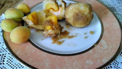 Marillenknödel aus Topfenteig liegen auf einem Teller, mit aufgeschnittenen, saftigen Aprikosen und einigen ganzen Früchten daneben.