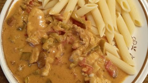Zartes Geschnetzeltes in cremiger Paprika-Rahm-Soße wird neben al dente Penne auf einem weißen Teller serviert.