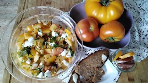 Bunte Tomatensalat mit Büffelmozzarella in einer Schüssel, umgeben von frischen Tomaten und knusprigem Brot auf einem Holzbrett.