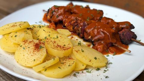 Saftige Fleisch-Spieße liegen neben Scheiben von gekochten Kartoffeln, beide mit Currysoße und Gewürzen garniert.