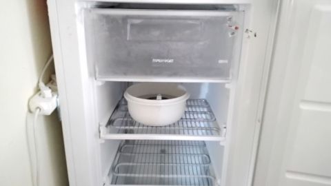 Ein Gefrierschrank mit gestapelten Regalen steht geöffnet da, während eine Schüssel im oberen Fach darauf wartet, abgetaut zu werden.