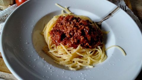 Spaghetti mit Bolognese-Soße sind auf einem Teller angerichtet, umgeben von frischen Tomaten und einer rustikalen Atmosphäre.