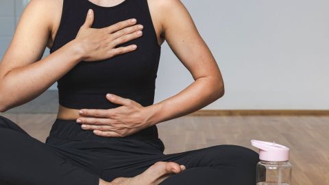 Eine sitzende Person führt eine Atemübung zur Entspannung durch, während ein Wasserkrug neben ihr steht.