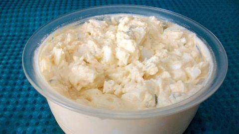 Ein cremiger Eiersalat ohne Mayo befindet sich in einer klaren Schüssel auf einer blauen Unterlage.