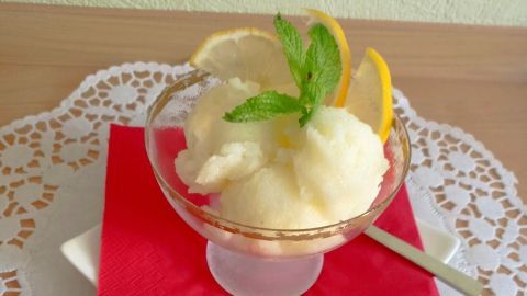 Ein Glas Zitronen-Sorbet steht auf einem roten Teller, dekoriert mit Zitronenscheiben und Minze auf einer Spitzendecke.