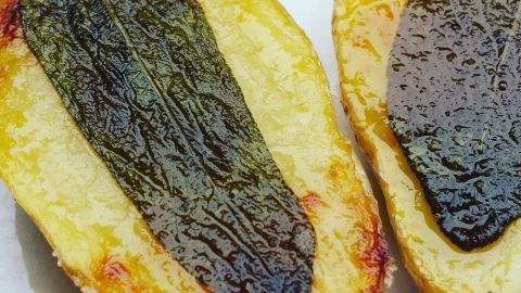 Zwei goldbraun gebratene Kartoffelhälften liegen auf einem Teller, garniert mit knusprigem, grünem Salbeiblatt.