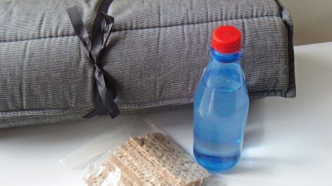 Eine Decke und eine Flasche Wasser liegen neben einer Tüte mit Keks auf einem Tisch, ideal für das Übernachten im Auto.