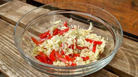 Ein klarer Glasschüssel enthält einen bunten Salat aus Weißkraut und Paprika, frisch zubereitet und knackig, auf einer hölzernen Oberfläche.