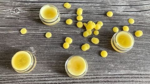 Kleine Gläser mit Lippenbalsam und gelben Wachskugeln sind auf einem rustikalen Holzuntergrund verteilt.