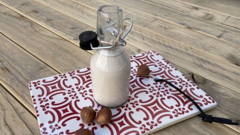 Ein Glas mit Haselnussmilch steht auf einem dekorativen Brett, umgeben von Haselnüssen auf einem Holztisch.