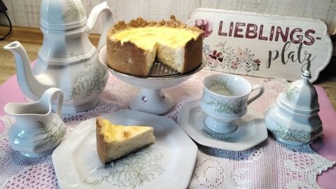 Ein Zitronen-Käsekuchen ist auf einem eleganten Teller platziert, umgeben von feinem Porzellan und einem handgeschriebenen Schild.