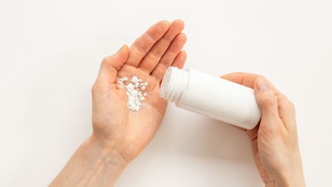 Eine Hand hält eine Flasche, während das Pulver in die andere Hand rieselt; ideal zur Behandlung von Hautreizungen durch Schwitzen.