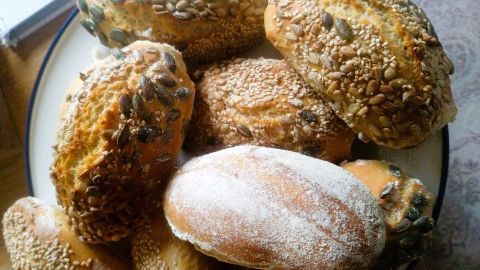 Krosse Frühstücksbrötchen mit verschiedenen Saaten liegen auf einem Teller in einer hellen Küche.