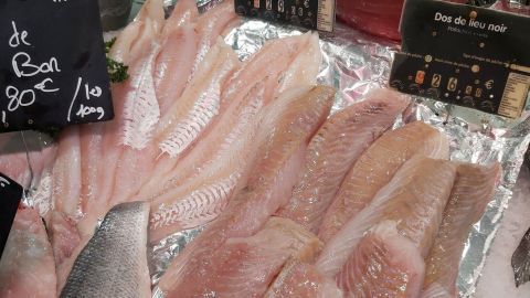 Frische Fischfilets liegen auf einem Eisteller, umgeben von Preisschildern und grüner Petersilie im Verkaufsbereich.