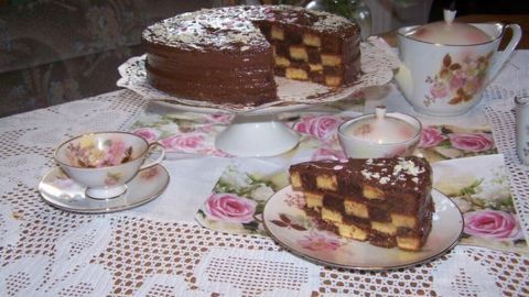 Eine Schachbrett-Torte steht auf einem Teller, während eine Portion auf einer Untertasse serviert wird, umgeben von Teetassen.