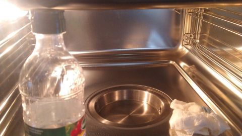 Eine flache Heizschale ist innen sichtbar, während eine Flasche Essig und ein Papiertuch zur Reinigung bereitstehen.