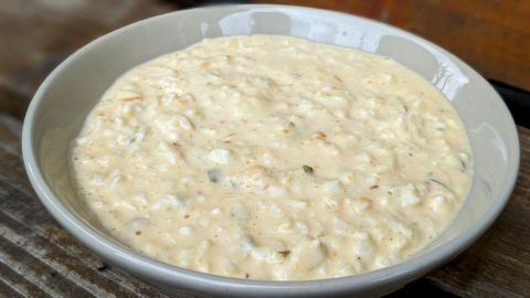 Eine Schüssel mit dänischer Remoulade steht auf einem rustikalen Holzuntergrund, cremig und appetitlich angerichtet.