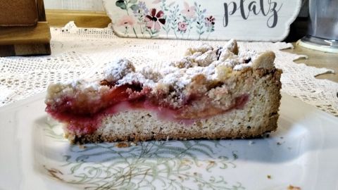 Ein Stück Zwetschgenkuchen liegt auf einem dekorativen Teller, staubzuckerbestäubt, in einer gemütlichen Umgebung mit einem einladenden Tisch.