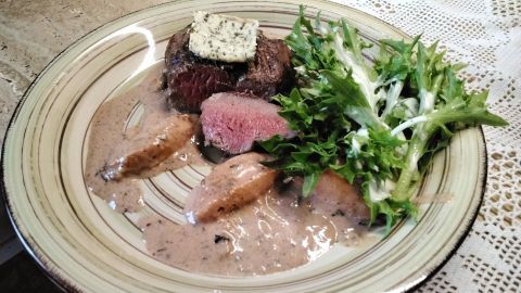 Zartes Rinderfilet mit Zwetschgensauce und frischem Salat auf einem eleganten Teller, serviert auf einem Tisch.