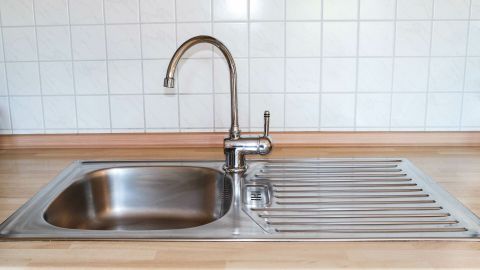 Ein glänzendes Spülbecken steht bereit zum Reinigen. Die Umgebung ist eine moderne Küche mit Fliesen und Holz.