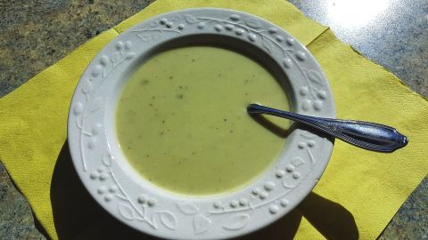 Ein Teller cremiger Rosenkohlsuppe steht auf einem gelben Tisch. Die Suppe hat eine glatte, grüne Textur.