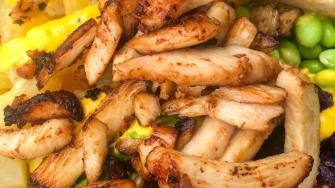 Gegrillte Hähnchenstreifen liegen über einem bunten Gemüsemix aus Reis, Ananas und grünen Erbsen in einer Schüssel.