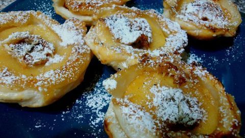 Gebackene Apfelringe sind auf einem blauen Teller angeordnet, bestäubt mit Puderzucker und goldbraun gebacken.