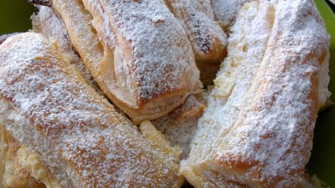 Leckere Blätterteigteilchen mit Vanillecreme sind üppig mit Puderzucker bestäubt und liegen auf einem grünen Teller.