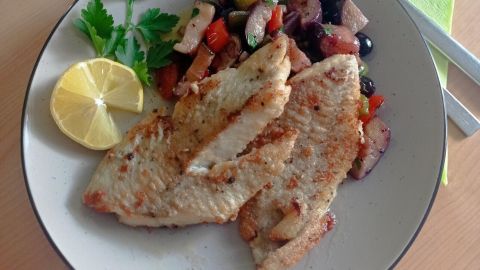 Zart gebratener Seelachs liegt auf einem Teller, umgeben von buntem Ratatouille und einem Zitronenschnitz.