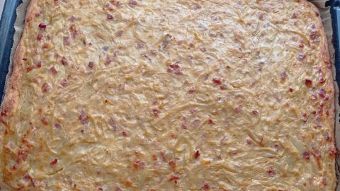 Ein goldbrauner Zwiebelkuchen auf einem Blech, frisch gebacken und nach dem Auskühlen bereit zum Servieren.