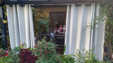 Der Sichtschutz aus hellen Stoffbahnen trennt die Terrasse vom Garten und schafft einen privaten, gemütlichen Raum.