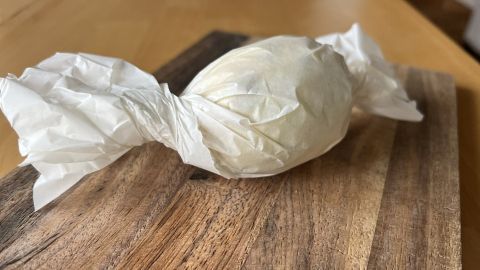 Eine weiß eingewickelte Zitrone ruht auf einem rustikalen Holztisch, umgeben von natürlichem Licht.