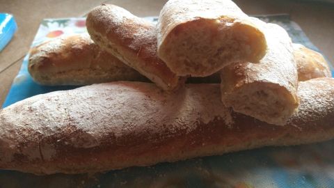 Frische Frühstücksbaguettes liegen auf einer bunten Unterlage. Die Baguettes sind leicht bestäubt und zeigen eine knusprige Oberfläche.