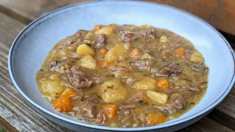 Ein herzhaftes, braunes Irish Stew mit Fleisch, Kartoffeln und Karotten in einer weißen Schüssel auf einem Holztisch.