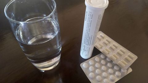 Ein Glas Wasser steht neben einer Pillenpackung und einer Röhrchen mit Tabletten, bereit zum einfachen Schlucken.