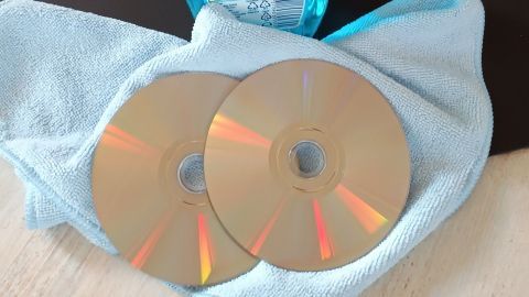 Zwei CDs liegen auf einem blauen Tuch, während eine Sprühflasche zum Reinigen bereitsteht.