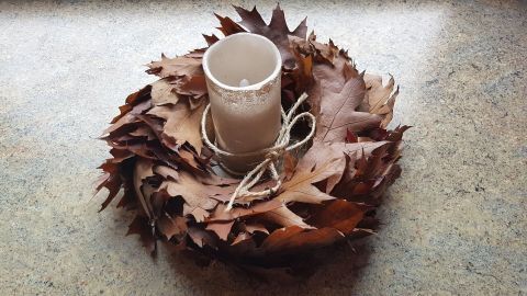 Ein Herbstkranz aus Eichenlaub liegt auf einer Tischoberfläche, in dessen Mitte eine Kerze gebunden ist.