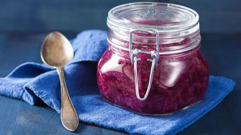 Ein Glas mit eingelegtem Rotkohl steht auf einem blauen Tuch, während ein Löffel daneben liegt.