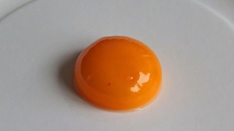 Ein glänzendes Eigelb liegt auf einem weißen Teller und ist bereit, als natürliche Maske gegen Pickel verwendet zu werden.