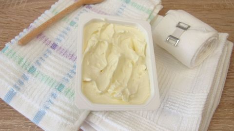 Ein Becher mit Quark liegt auf einem Tisch, begleitet von einem Holzlöffel und Wickelmaterial für die Anwendung.