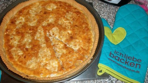 Ein frisch gebackener schwäbischer Zwiebelkuchen liegt auf einem Blech und wird von einem Ofenhandschuh begleitet.