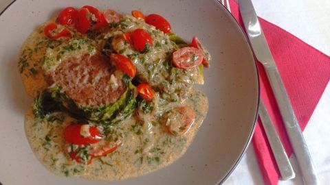Eine köstliche Wirsingroulade liegt auf einem Teller in Sahnesauce, begleitet von gebratenen Kartoffeln in einer Schüssel.