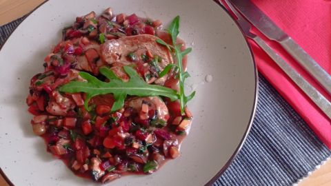 Saftige Kalbsfilet-Scheiben liegen auf einer bunten Gemüsemischung, dazu Brezeln in einer Schüssel im Hintergrund.