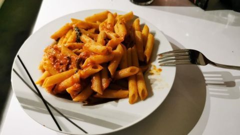 Penne liegen appetitlich in einer Schüssel, überzogen mit Tomatensoße, umgeben von einem eleganten Tischsetting.