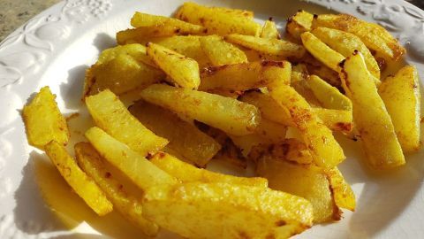 Kohlrabi-Pommes liegen knusprig und goldbraun auf einem weißen Teller und wirken appetitlich im Sonnenlicht.