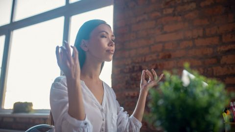 Eine Frau meditiert entspannt in einem modernen Büro, um Stress abzubauen und ihre innere Ruhe zu finden.